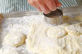Biscuit dough with a hand holding a biscuit cutter.