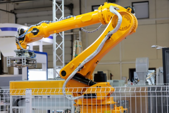 A yellow robotic arm of an automatic robotic palletizer system in a short cage inside of a warehouse.
