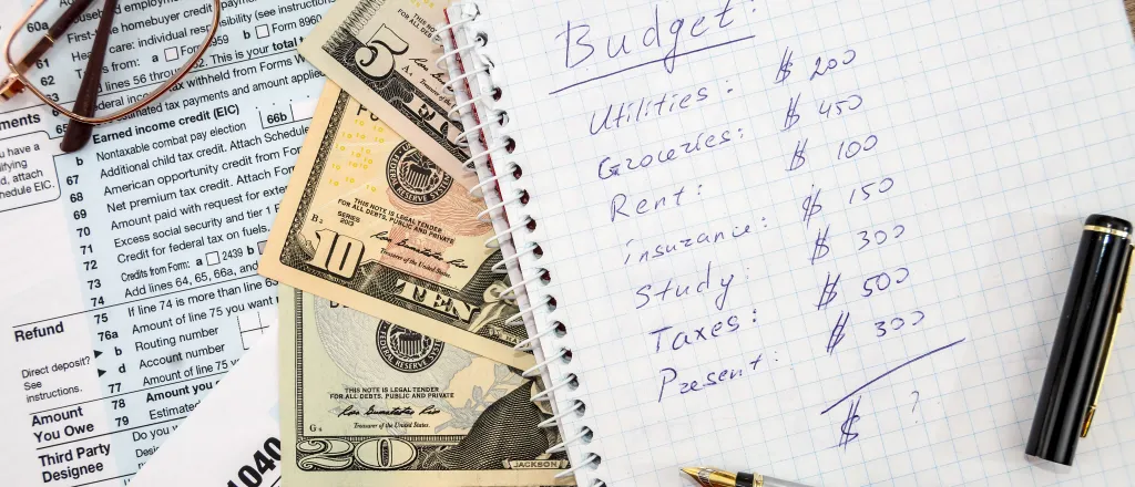 PROMO HIRES Finance - Budget Money Tax Forms - iStock - alfexe Notebook with a pen on a page showing a personal budget. Underneath are paper currency and tax forms. Eyeglasses are nearby