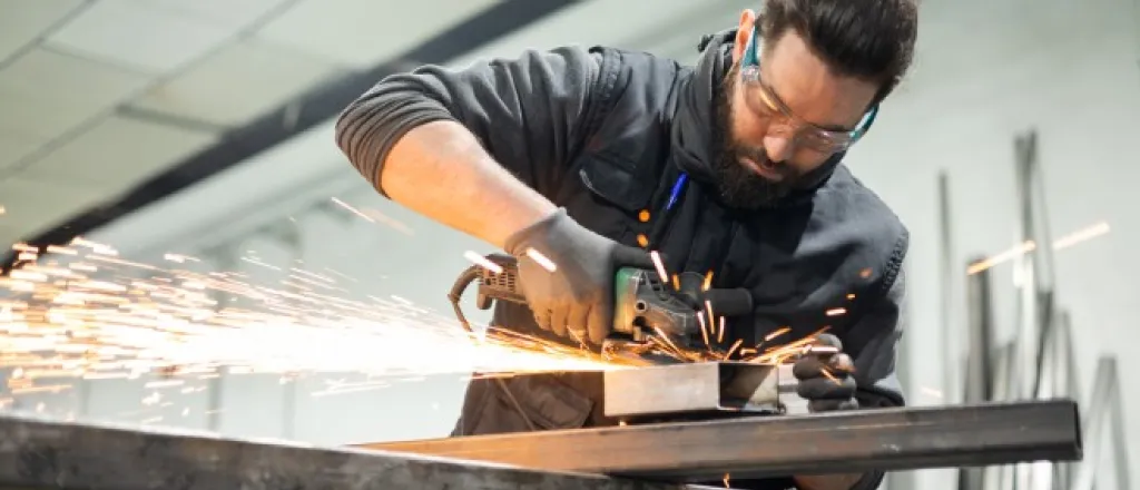 Safety Tips When Operating a Glass Grinder Machine A man working hard in a machine shop with a glass grinder machine and sparks flying. He's wearing proper PPE.