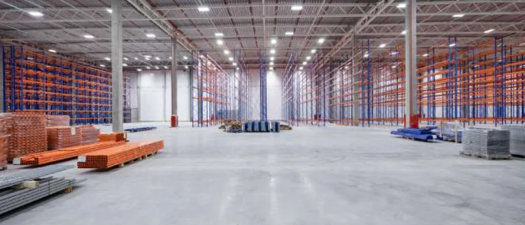 A large empty warehouse with high beam, LED lights. There are empty blue and orange rafters for inventory. A large empty warehouse with high beam, LED lights. There are empty blue and orange rafters for inventory.