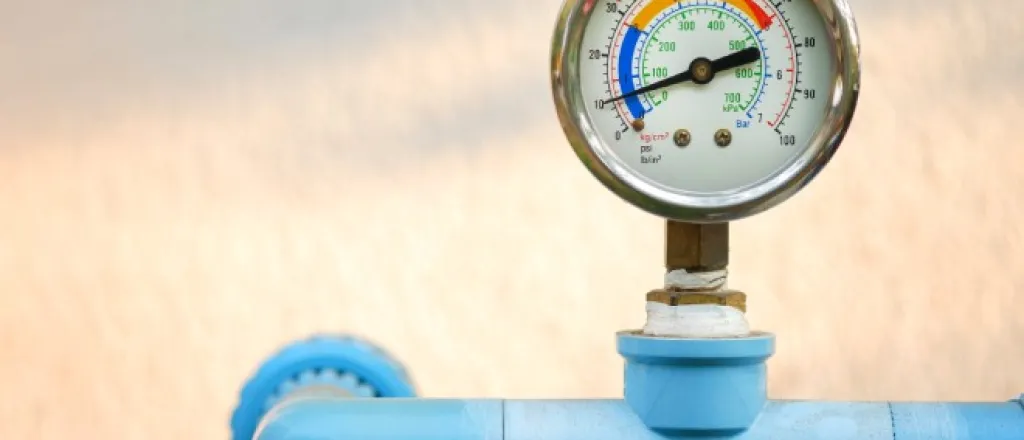 Different types of industrial pressure gauges A pressure gauge with metal casing attached to a bright blue pipeline connected to an off-white wall.
