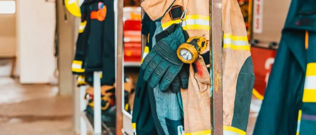 Fire-resistant clothing for firefighters, including jackets and gloves, hanging from a rusty metal rack. Fire-resistant clothing for firefighters, including jackets and gloves, hanging from a rusty metal rack.