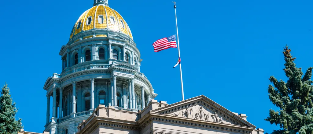 PROMO HIRES Flag - Half Staff Mast Colorado Capitol US United States - iStock - RoschetzkyIstockPhoto View of the Colorado state capitol entrance and dome, with United States and Colorado flags at half staff
