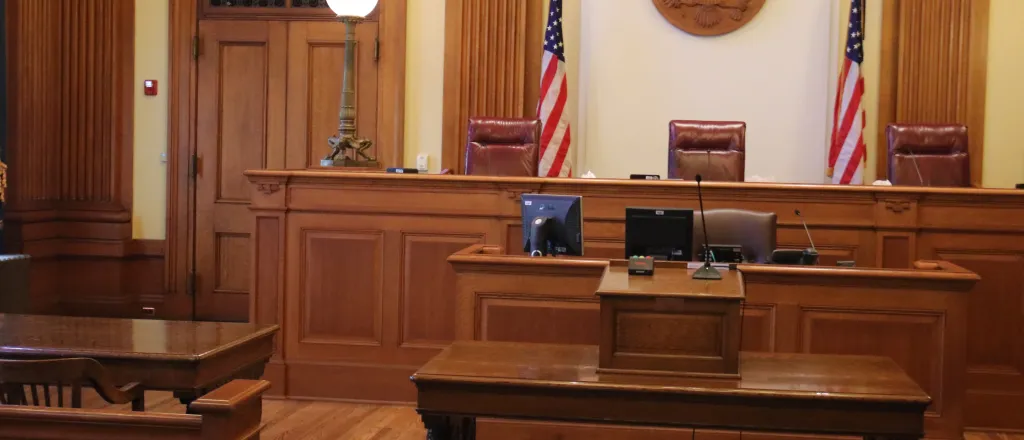 PROMO HIRES Legal - Court Room Justice Law - iStock - keeton12 Scene of a courtroom facing the judges' bench flanked by two United States flags