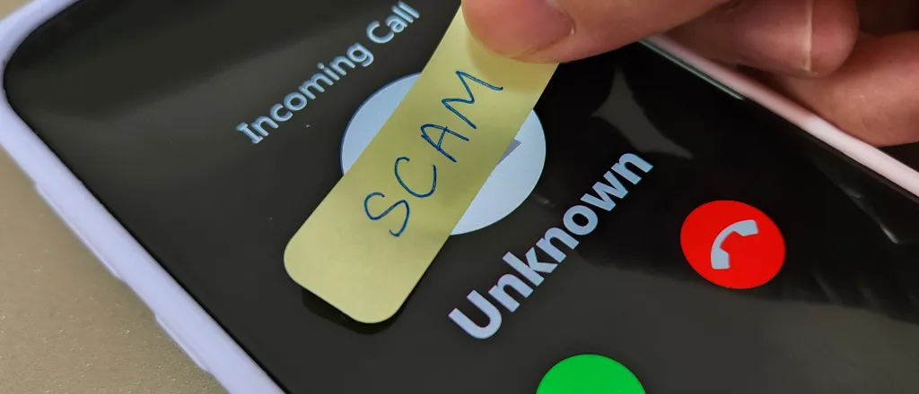 PROMO HIRES CROPPED Technology - Communication Cell Phone Scan Call Crime - celiaosk - Stock-1741822335 Smartphone showing an incoming call from an unknown number. Fingers are placing a hand-written label with the word "scam" over the top.