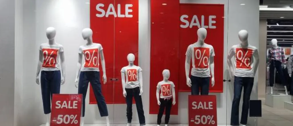 Manequins in white shirts with a red box with % signs in them surrounded by sale signs that advertise 50% off. Manequins in white shirts with a red box with % signs in them surrounded by sale signs that advertise 50% off.