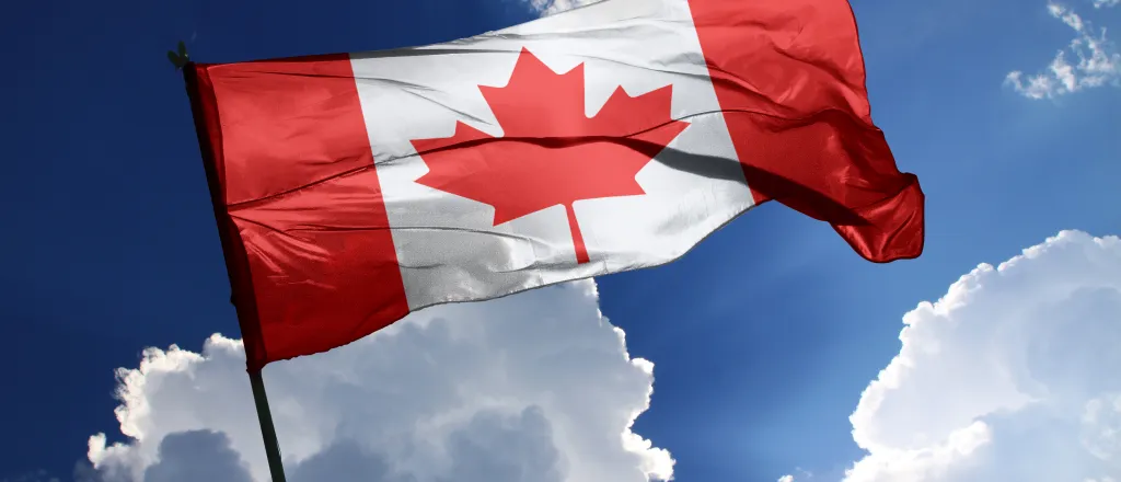 PROMO HIRES Flag Canada Canadian Trade - Aoraee - iStock-1738961163 Flag of Canada against a partly cloudy, sunlit sky