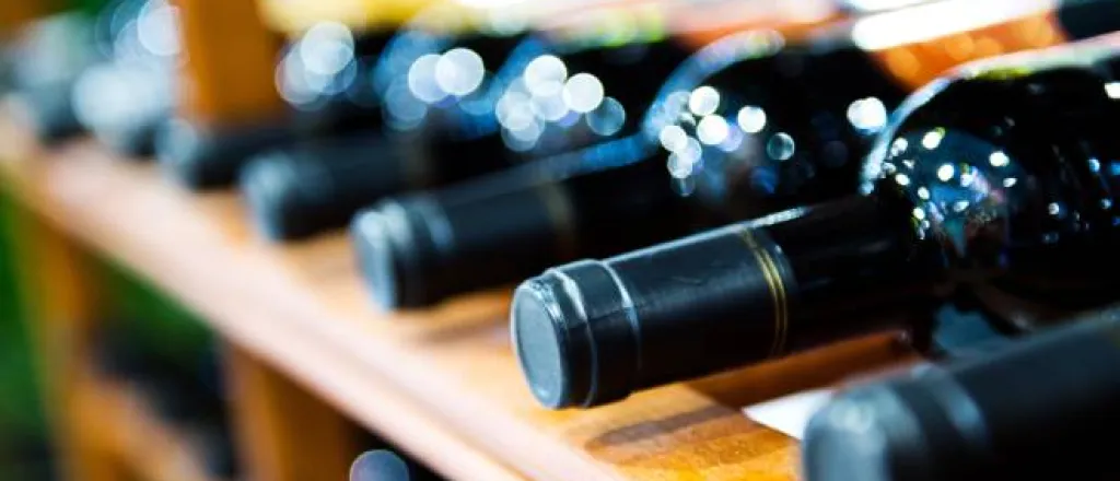 An extreme close-up view shows several dark-colored wine bottles lying on a wooden wine storage rack. An extreme close-up view shows several dark-colored wine bottles lying on a wooden wine storage rack.