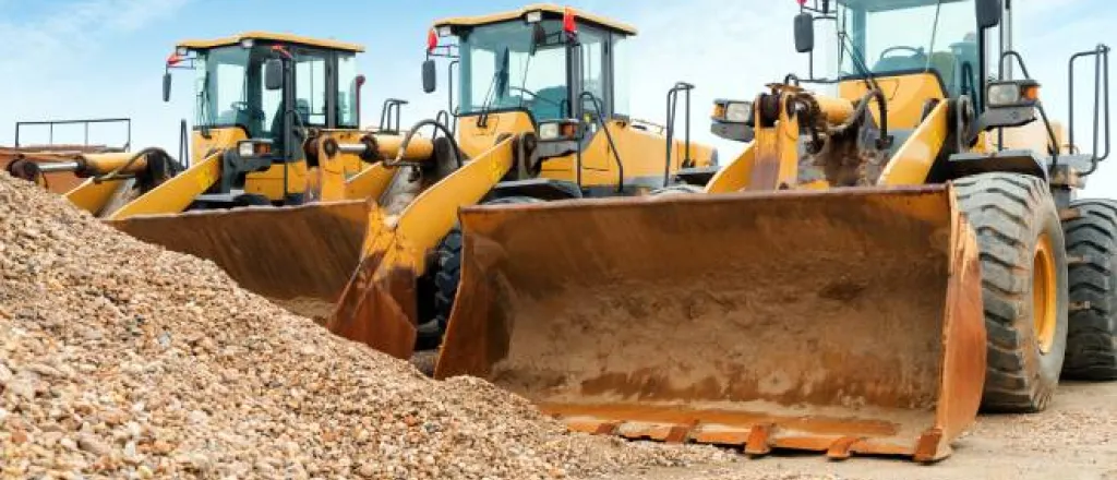 Three large orange and black excavators parked next to each other in front of a pile of rubble on a sunny day. Three large orange and black excavators parked next to each other in front of a pile of rubble on a sunny day.