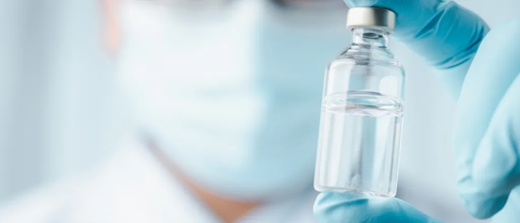 A scientist wearing a blue latex glove holding a small glass sample vial filled with a clear liquid in front of his face. A scientist wearing a blue latex glove holding a small glass sample vial filled with a clear liquid in front of his face.