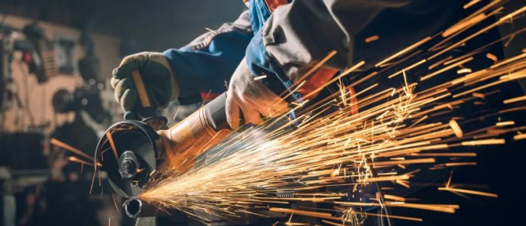A metalworker using a saw to cut something. The worker is in safety gear and there are sparks flying back at them.