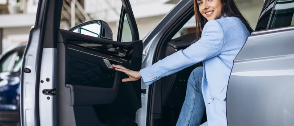 Things To Know Before Accepting a Company Car A woman in a blue suit jacket sits in the front seat of a silver car with the door open.