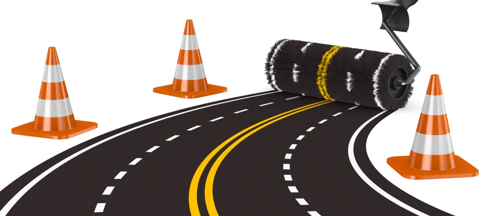 PROMO HIRES CROPPED Transportation - Road Construction Cone Zone - ISerg - iStock-1333705544 Concept image of a paint roller creating a four-lane road. Construction cones are at the sides.