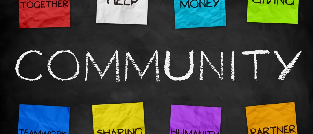 Word "Community" written on a chalkboard, with eight colored paper notes above and below reading "togetherness, help, money, giving, teamwork, sharing, humanity, and partner"