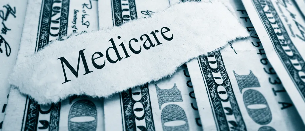 PROMO HIRES Finance - Government Medicare Words Budget Money Cash - zimmytws - iStock-527631529 A scrap of torn paper with the word "Medicare" rests on top of a spread of United States 100 dollar currency.