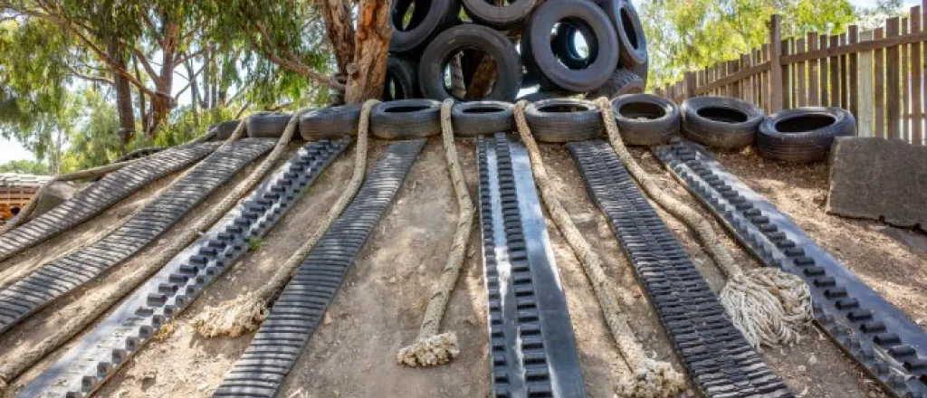 An outdoor play space with recycled materials, such as tires, rope, and metal hardware. The play space is on a dirt incline.