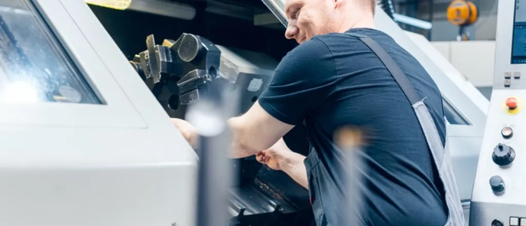 Decisions To Make When Your Tooling Budget Is Small A professional tooling machine worker in a warehouse. They're smiling as they work on a tooling project inside the machine.
