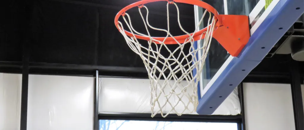 Basketball in the air approaching a basket. A scoreboard is in the background.