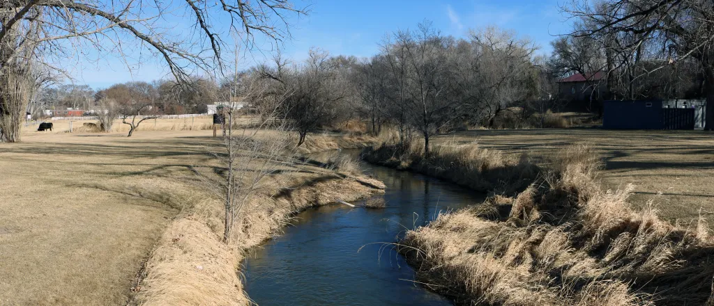 View of a small river winding through an open area with trees in the distance.