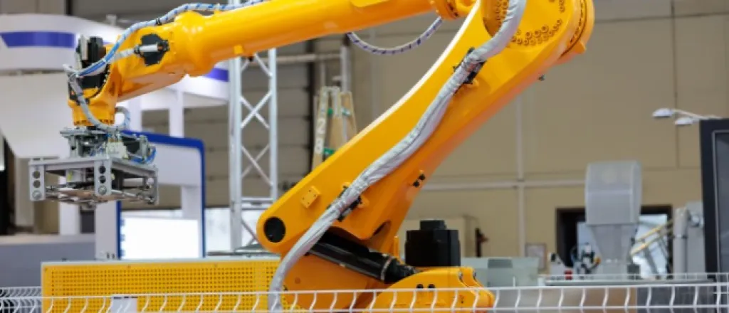 A yellow robotic arm of an automatic robotic palletizer system in a short cage inside of a warehouse.