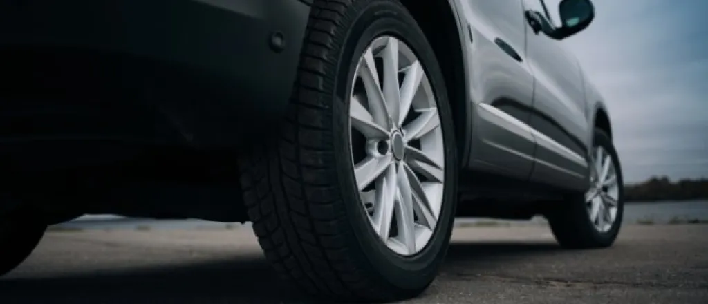 A close-up view from the ground of the rear wheel and tires of a grey SUV parked on pavement on a cloudy day.
