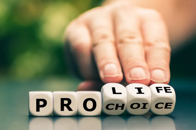 Dice with letters spelling out "Pro Life" and "Pro Choice." A hand tilts the dice to show "Life" and "Choice."