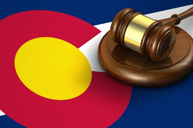 Gavel resting on a strike plate on top of a Colorado state flag.