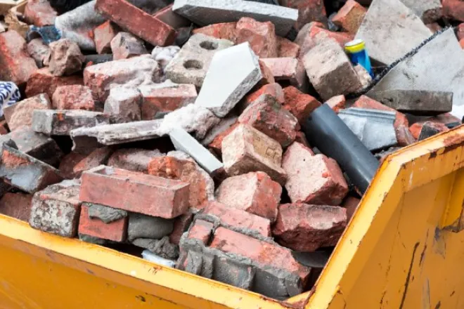 Close-up of a yellow dump truck bed. The bed is full of bricks of various sizes and colors, as well as other debris.