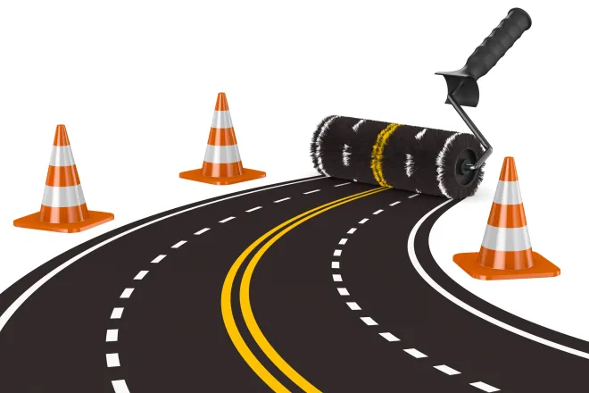 Concept image of a paint roller creating a four-lane road. Construction cones are at the sides.