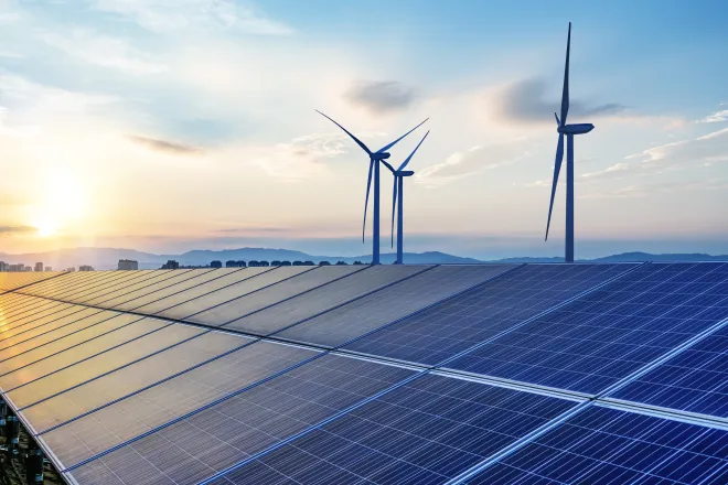 Solar panels with wind turbines in the background.