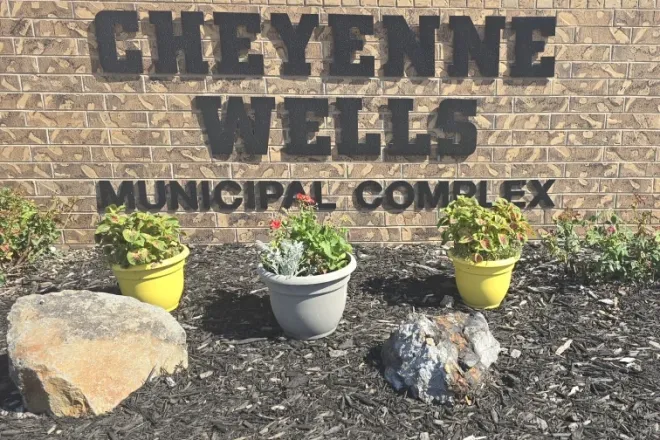Brick wall with the words Cheyenne Wells Municipal Complex. Assorted potted plants and rocks are on mulched ground in front of the sign.