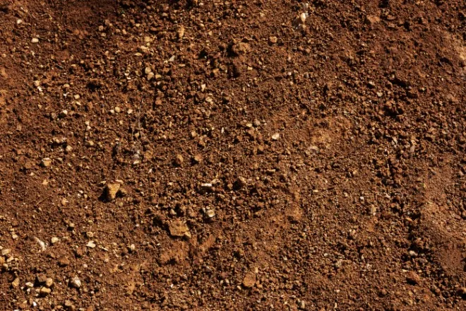 A close view of uneven red soil with small rocks and pebbles scattered unevenly across a rough, dry ground surface.