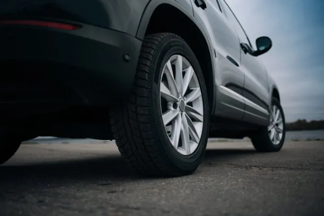 A close-up view from the ground of the rear wheel and tires of a grey SUV parked on pavement on a cloudy day.