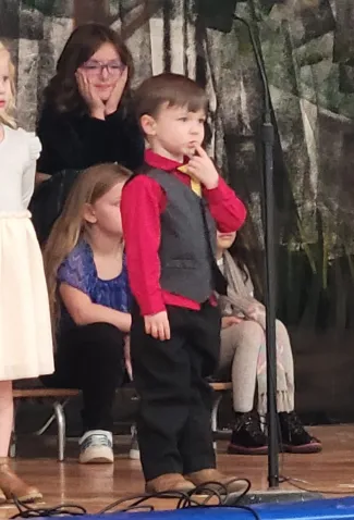 Child performing on a stage while people look on.