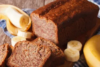 Banana Bread - USDA Partly sliced loaf of banana bread surrounded by parts of bananas.