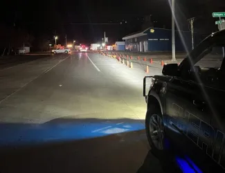 Night view of a closed road and vehicles with traffic cones marking spilled diesel.