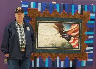 Man standing next to a quilt.