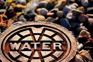 PROMO HIRES Water Pipe Cover Manhole Drought - artzenter - iStock-509493427 Metal cover labeled "water" at ground level.