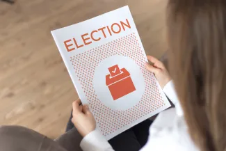 PROMO HIRES Politics - Election Guide Booklet Vote Ballot - iStock - relif Person holding a booklet titled "Election"
