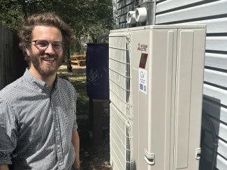 James Warren in West Denver with air-source heat pump - BigPivots.com - Allen Best Man standing next to an air-source heat pump.