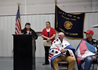 2024 American Legion Post #125 Dinner - Roland Sorensen. Ceremony to present quilts to veterans. Two speakers are standing, and two recipients are seated.