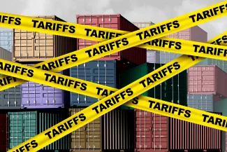 PROMO HIRES CROPPED Trade - Tariffs Shipping Transportation Taxes Politics - wildpixel - iStock-2189862167 Artist's representation of cargo shipping containers with yellow banners in front labeled with the word "tariff"