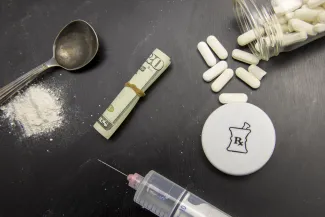 PROMO HIRES Health - Drugs Cash Opioids Needle Syring - karenfoleyphotography - iStock-832280392 Overhead view of white powder next to a spoon, hypodermic syringe and needle, a rolled up United States 20 dollar bill with rubber band around it, and an open pill bottle with the contents partially spilled.