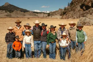 A large group of people standing in open space facing the camera. Mountains are in the background.