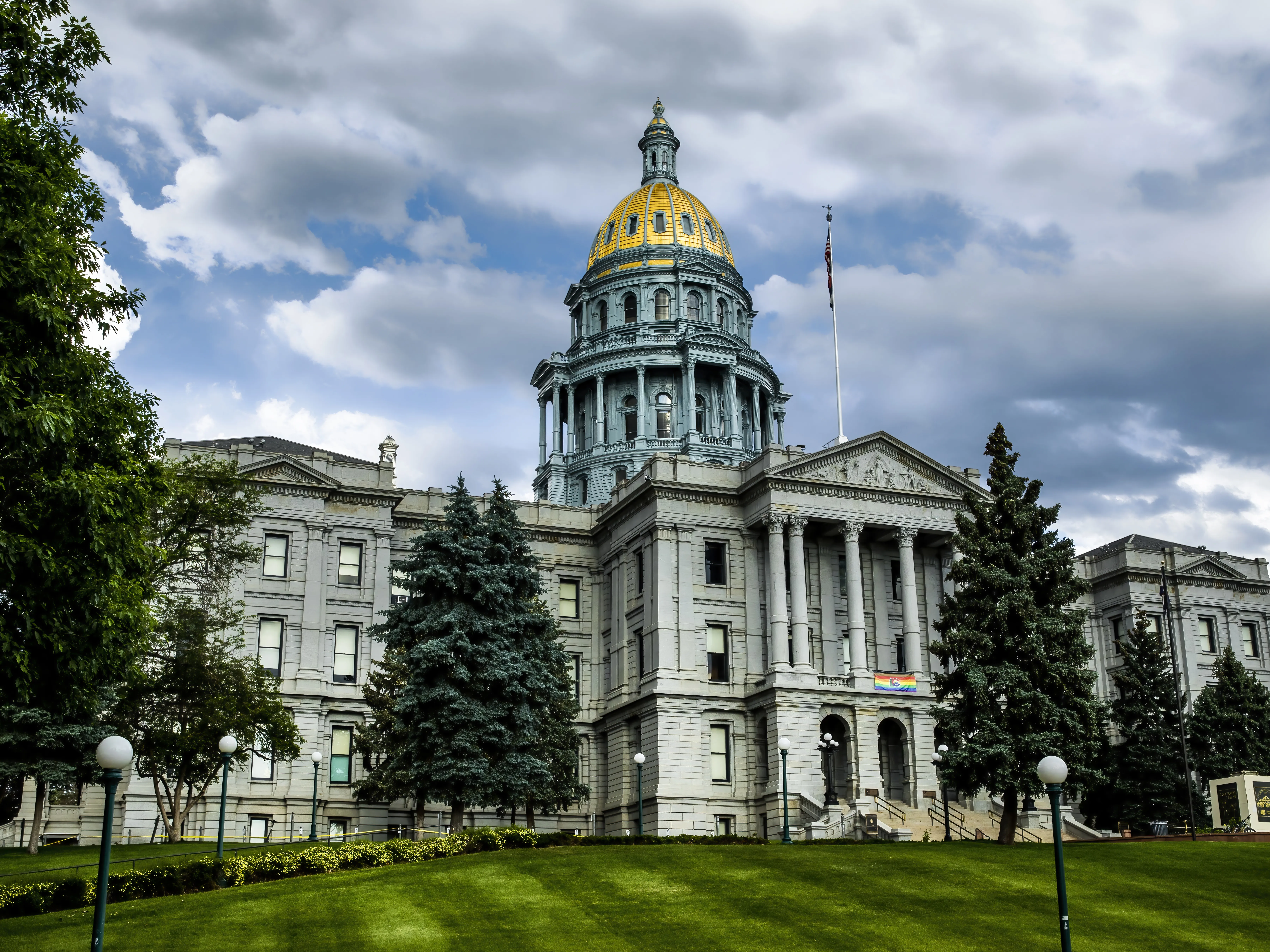 Colorado State Capitol Building fronted by green trees under a cloudy sky