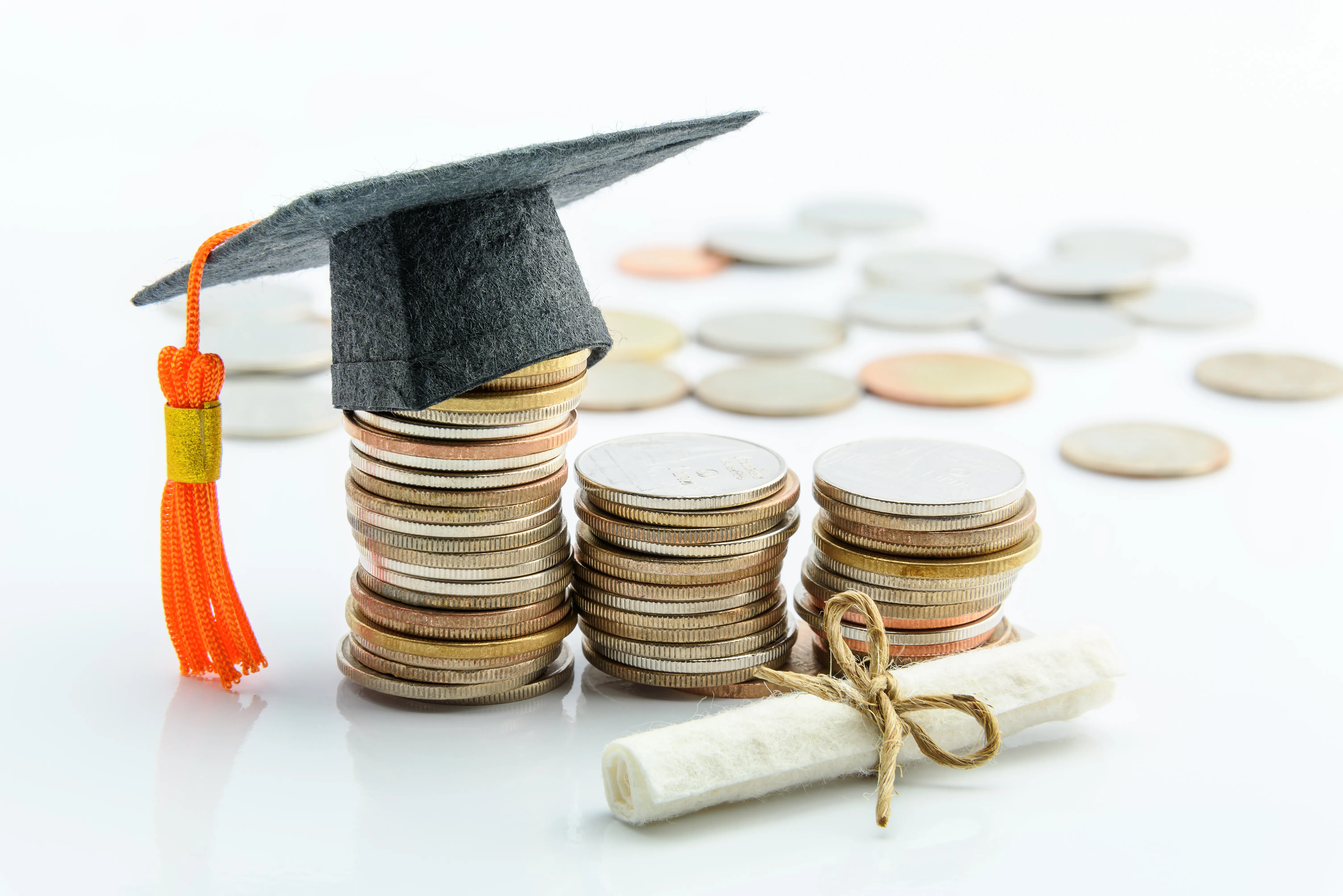 Stacks of coins with miniature mortar board on top and miniature rolled diploma in front