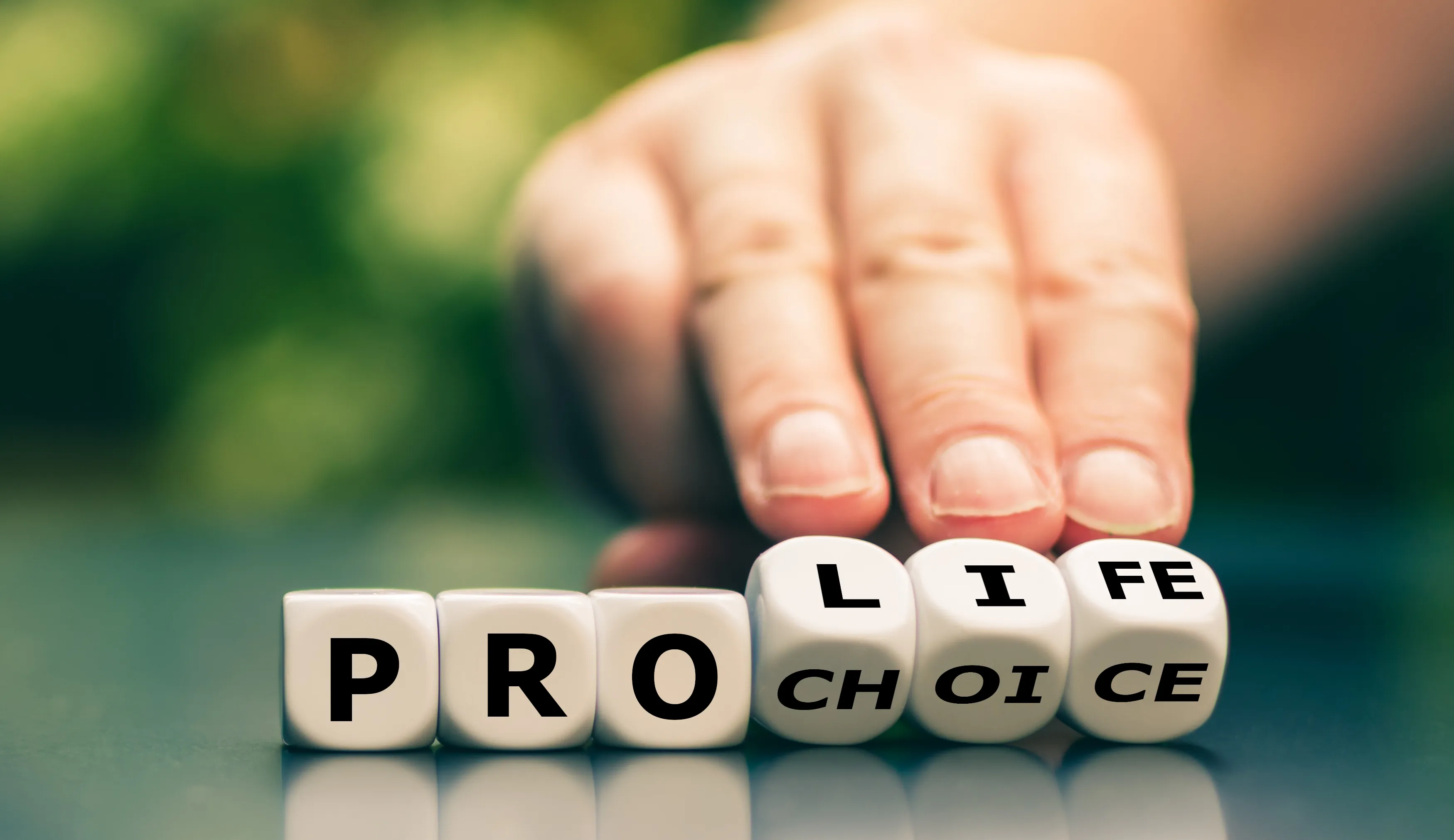 Dice with letters spelling out "Pro Life" and "Pro Choice." A hand tilts the dice to show "Life" and "Choice."