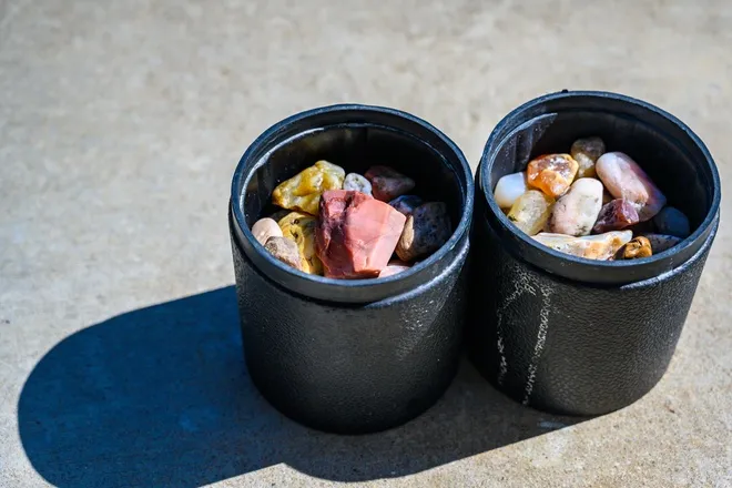 Two rubber rock tumbling barrels are placed on the ground and filled with different minerals in varying sizes.