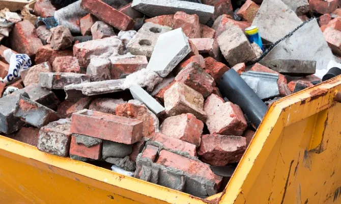 Close-up of a yellow dump truck bed. The bed is full of bricks of various sizes and colors, as well as other debris.